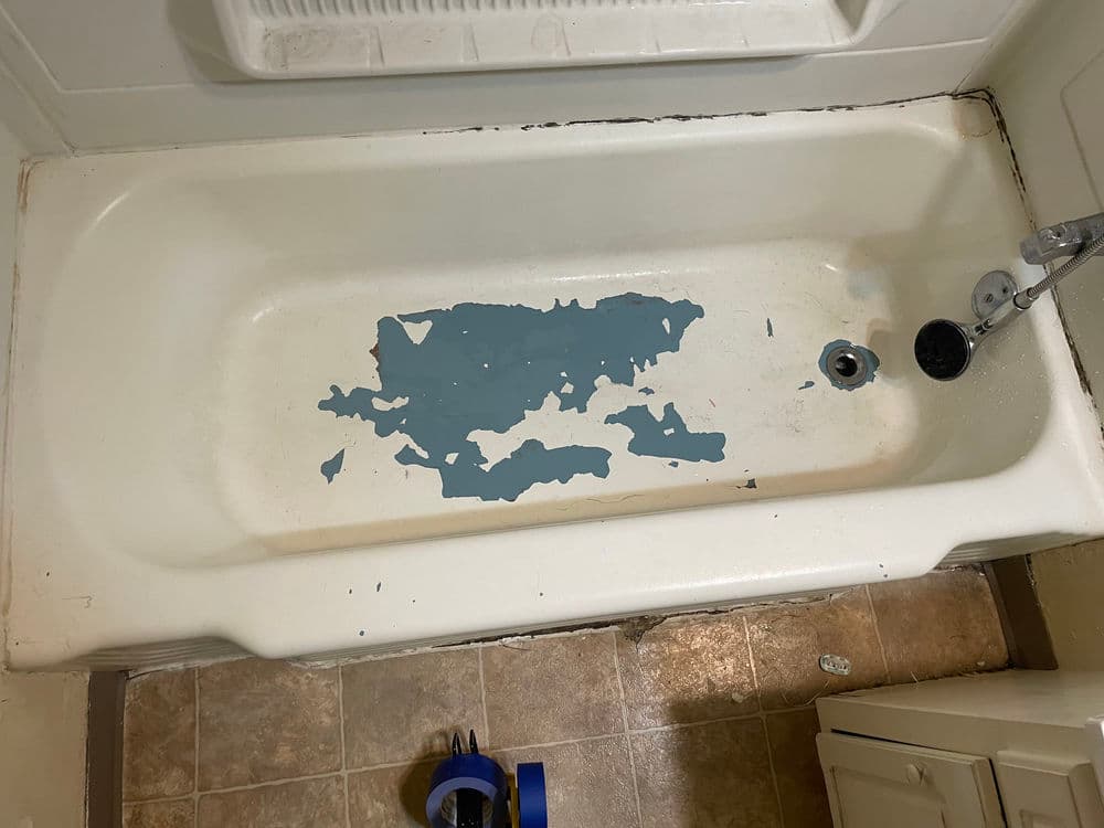 Bathtub with peeling blue paint and visible damage, ready for renovation.